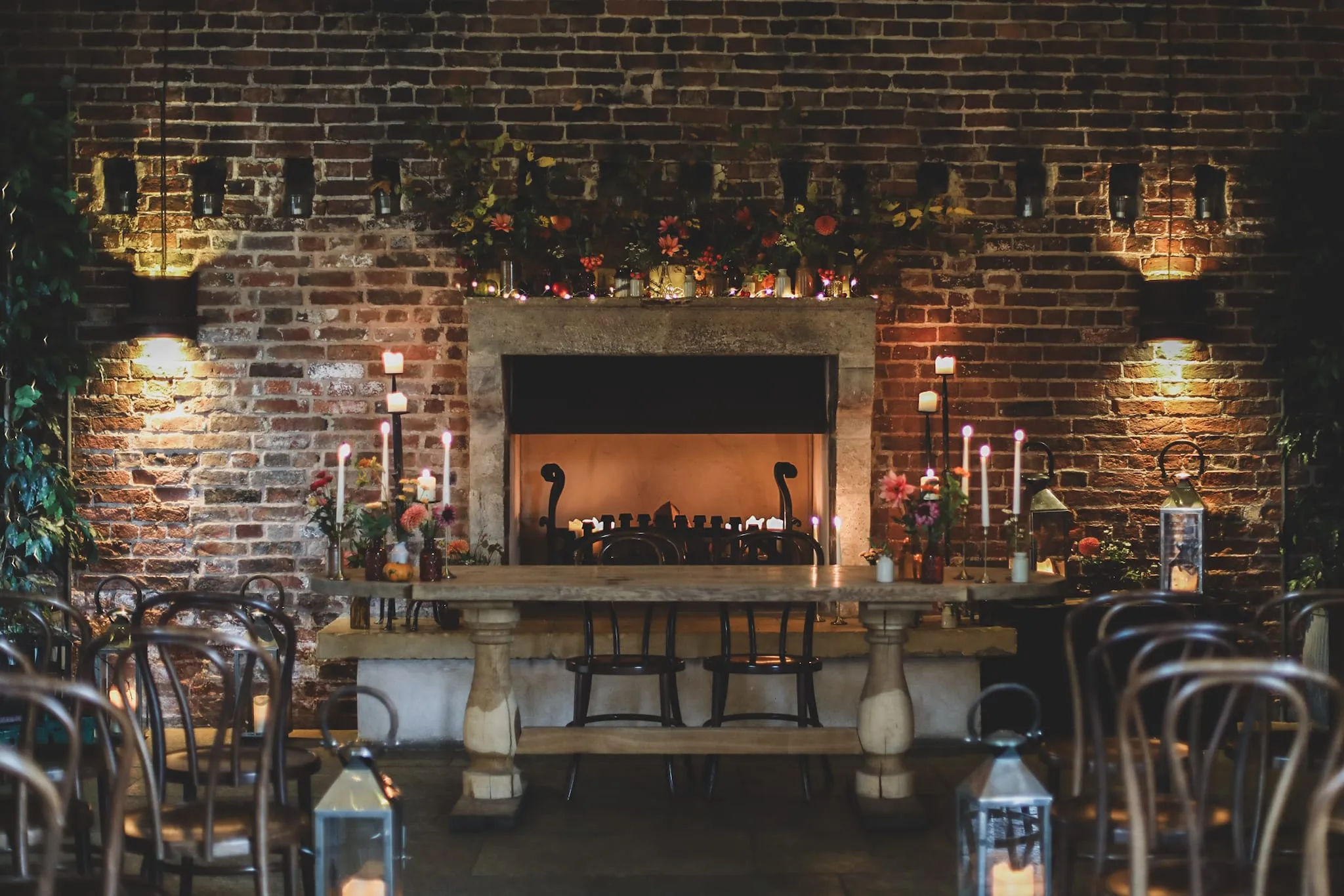 A candlelit wedding table in front of a brick fireplace, dressed with seasonal flowers